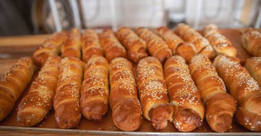 Hamura sarılmış sosisli börekler ve susam tohumları.