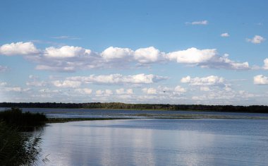 Durgun su yüzeyi mavi gökyüzünün altında beyaz bulutlar ve uzak ufuklarla