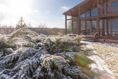 Güneşli kış sabahında karla kaplı bahçeli modern ahşap kır evi.