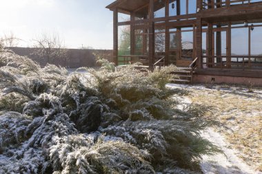 Güneşli kış sabahında karla kaplı bahçeli modern ahşap kır evi.