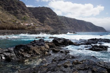 Turkuaz okyanus suyu, karanlık volkanik kayaların arasında doğal kıyı manzarası.