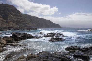 Güçlü okyanus dalgaları engebeli volkanik kıyılarda kırılıyor. Gücü simgeliyor.