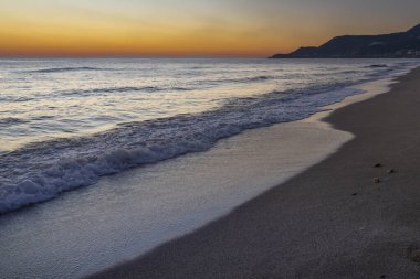 Akdeniz dalgası, Alanya Türkiye kıyılarında renkli günbatımında kumlu plajı yıkıyor.