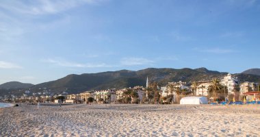 Alanya 'da palmiye ağaçları ve dağları olan güneşli kumlu sahil, Türkiye' nin kıyı beldesi manzarası.