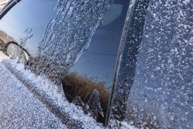 Soğuk kış sabahında, kar ve buzla kaplı araba güneş ışığıyla parıldıyor.