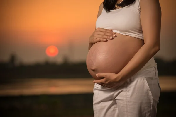 Pregnant woman relaxing lakeside sunset background — Stock Photo, Image