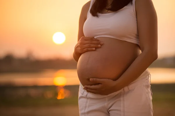 Pregnant woman relaxing lakeside sunset background — Stock Photo, Image