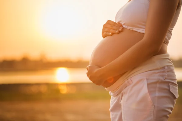 Pregnant woman relaxing lakeside sunset background — Stock Photo, Image