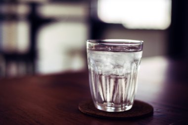 Drinking cold water into a glass placed on the wooden table.