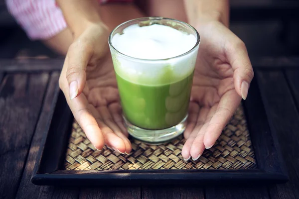 Woman holding Matcha green tea latte on wooden table — Stock Photo, Image