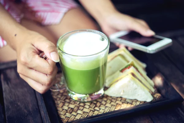 Mujer sosteniendo té verde Matcha café con leche y el uso de teléfono móvil — Foto de Stock