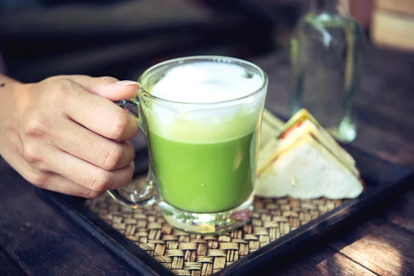 Woman holding Matcha green tea latte on wooden table — Stock Photo, Image
