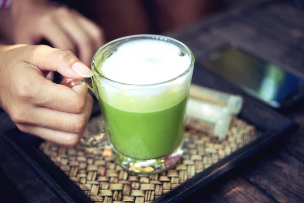 Woman holding Matcha green tea latte on wooden table