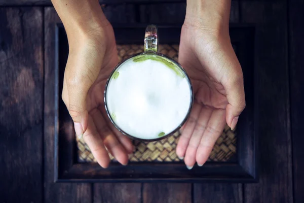 Mujer sosteniendo té verde Matcha con leche sobre mesa de madera —  Fotos de Stock