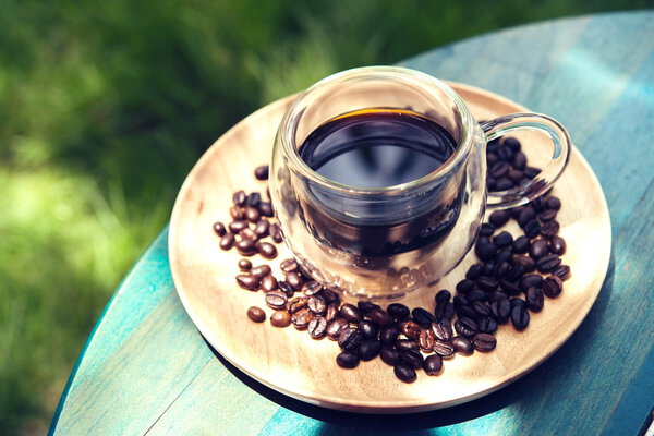 Hot Americano on wooden table green grass background