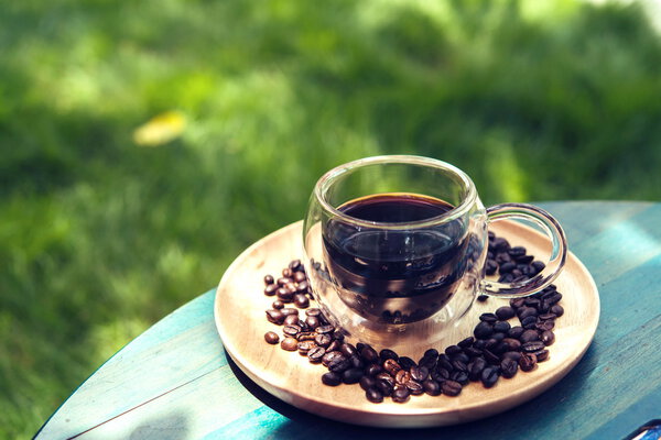 Hot Americano on wooden table green grass background