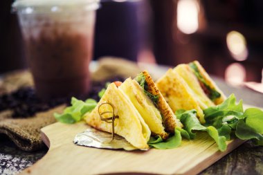 Ham sandwich and coffee laid on a wooden table.