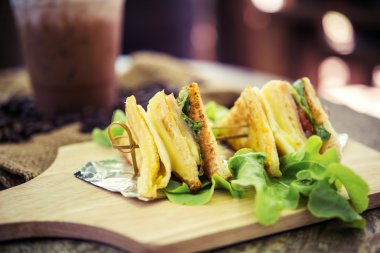 Ham sandwich and coffee laid on a wooden table.