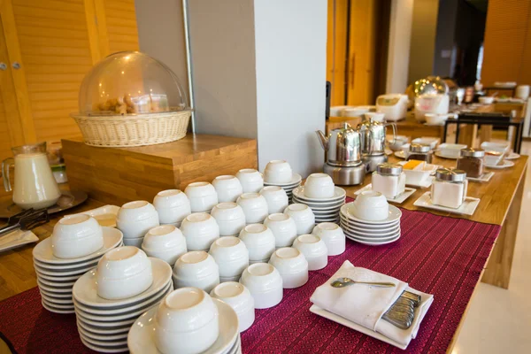 Cups, plates and utensils arranged on a white table and buffet b