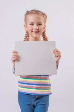 Renkli ceketli, saçları örgülü mutlu, sarışın bir kız ellerinde beyaz bir çarşaf tutuyor ve gülümsüyor.