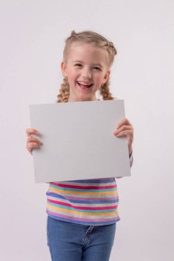 Renkli ceketli, saçları örgülü mutlu, sarışın bir kız ellerinde beyaz bir çarşaf tutuyor ve gülümsüyor.