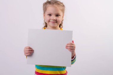 Renkli ceketli, saçları örgülü mutlu, sarışın bir kız ellerinde beyaz bir çarşaf tutuyor ve gülümsüyor.