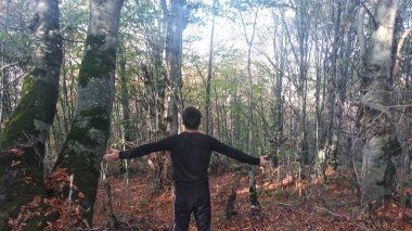 Yaşlı ağaçların arasında siyah takım elbiseli bir adam. Dua ediyor..