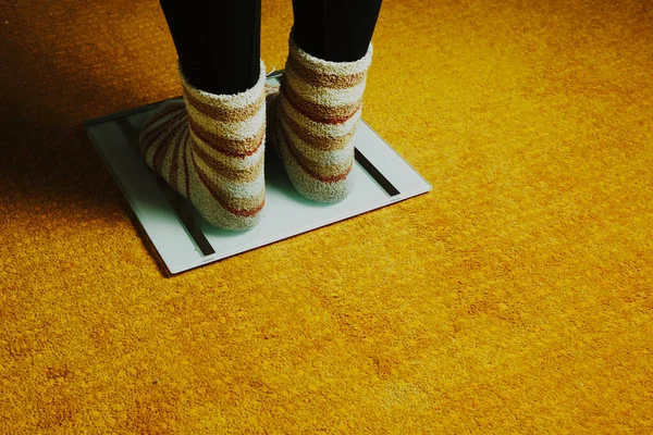 woman feet with socks and scales on yellow carpet