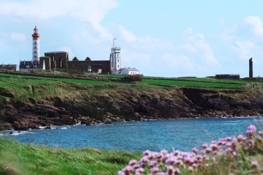 Deniz feneri manzarası ve yeşil çimen çiçekleri ve okyanus olan antik kilise kalıntıları. Brittany Fransa