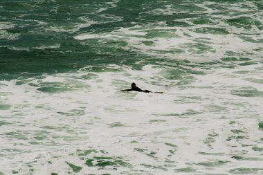 Gemideki sörfçü okyanus suyunda yüzer.