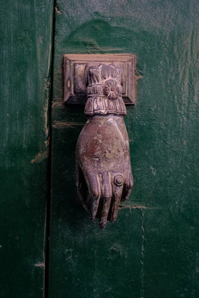 antique knock door shape hand on green door. Southern Italy.