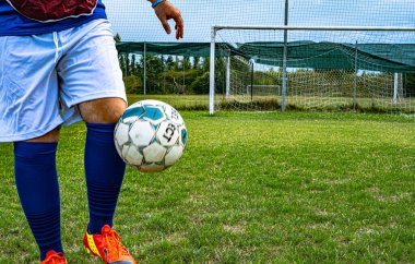 Futbolcunun ayağı futbol sahasında top sürüyor ve kalede gol var.