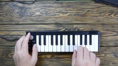 Midi klavyesinde çalıyor. Midi Klavyesi ahşap bir masada