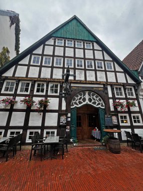 Osnabruk 'taki Aziz Peters Katedrali, gri gökyüzünün altında park halindeki arabalarla dolu ağaçlık bir meydanın üzerinde iki taş kule ve çizgili bir çatıyla yükselir..