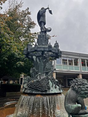 Osnabruk 'taki Aziz Peters Katedrali, gri gökyüzünün altında park halindeki arabalarla dolu ağaçlık bir meydanın üzerinde iki taş kule ve çizgili bir çatıyla yükselir..