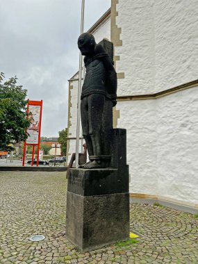 Kutsal bir heykel, Osnabruk 'taki bir kilisenin önündeki bir kaidede, acı ve hatırayı sembolize eden, taşa bağlanmış, ince bir figürü tasvir eder..