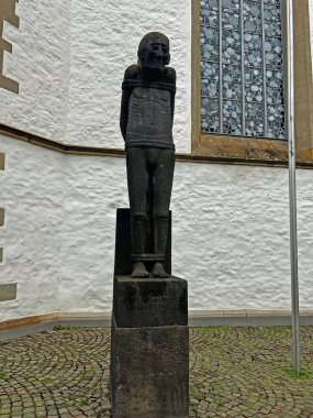 Kutsal bir heykel, Osnabruk 'taki bir kilisenin önündeki bir kaidede, acı ve hatırayı sembolize eden, taşa bağlanmış, ince bir figürü tasvir eder..