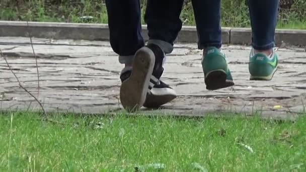 Jongen en meisje, zittend op een bankje en praten naar beneden. Bewolkt zomerdag. Langzaam lopen onder grote bomen in de buurt van de banken. Zitten op de Bank jongen en meisje. Stad landschap. De weg bedekt met stenen. — Stockvideo