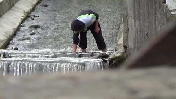 De kreek in het park. Jongen verzamelt munten in de creek park. Bewolkt zomerdag. Stad landschap. — Stockvideo