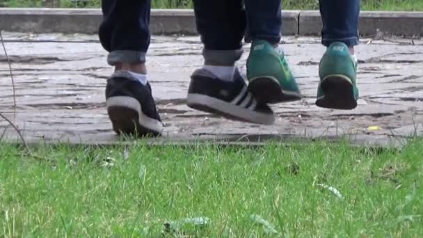 Garçon et fille assis sur un banc et parlant vers le bas.Jour d'été nuageux.Promenade lente parmi les grands arbres près des bancs. Asseyez-vous sur le banc garçon et fille.Paysage de la ville. La route couverte de pierres . — Video