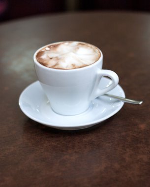 Masadaki beyaz bardakta kapuçino.