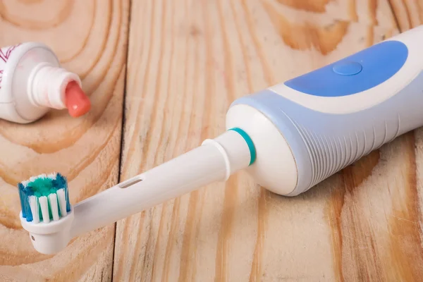 Electric toothbrush with a tube of toothpaste on  wooden background — Stock Photo, Image