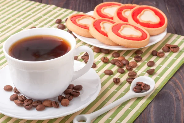Filiżanka kawy z fasoli i ciasteczka na drewnianym stole — Zdjęcie stockowe