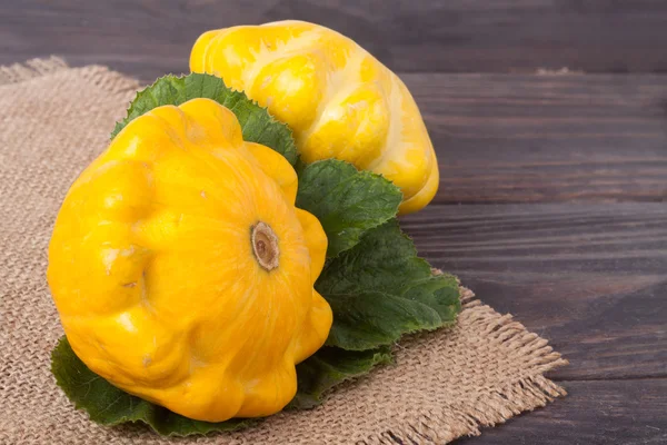 two yellow squash on a wooden background with napkin of burlap