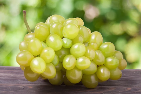 Cacho de uvas verdes maduras em uma mesa de madeira com fundo desfocado — Fotografia de Stock