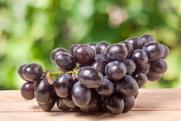 Racimo de uvas azules sobre una mesa de madera con fondo borroso — Foto de Stock