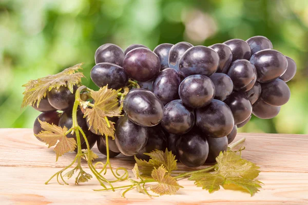 Racimo de uvas azules sobre una mesa de madera con fondo borroso — Foto de Stock