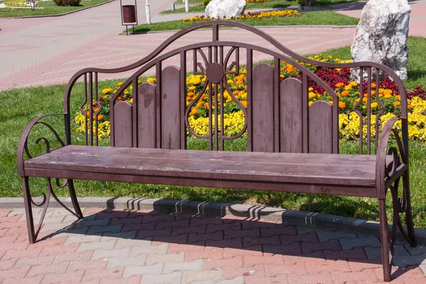 Holzbank auf einem Hintergrund aus Rasen mit Blumen — Stockfoto