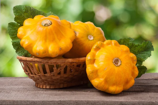 Žlutá pattypan squash s listy v proutěném koši na dřevěný stůl rozmazané pozadí — Stock fotografie