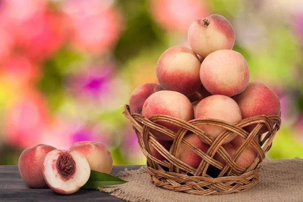 Персики в плетеной корзине на деревянном столе с размытым фоном — стоковое фото